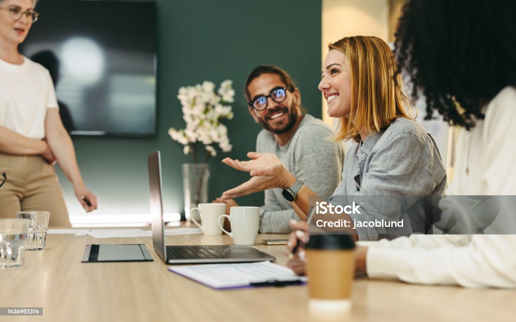 Business woman talking to her colleagues during a meeting in a boardroom. Group of happy business people working together in a creative office.